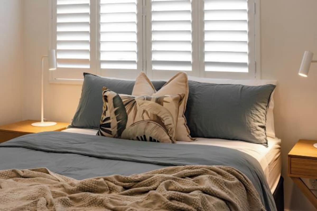 A bed with a blue and beige blanket, a pillow with a leaf pattern, and a bedside lamp.