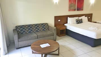 A hotel room with a bed, a sofa, a small wooden table, and two wall-mounted lights.