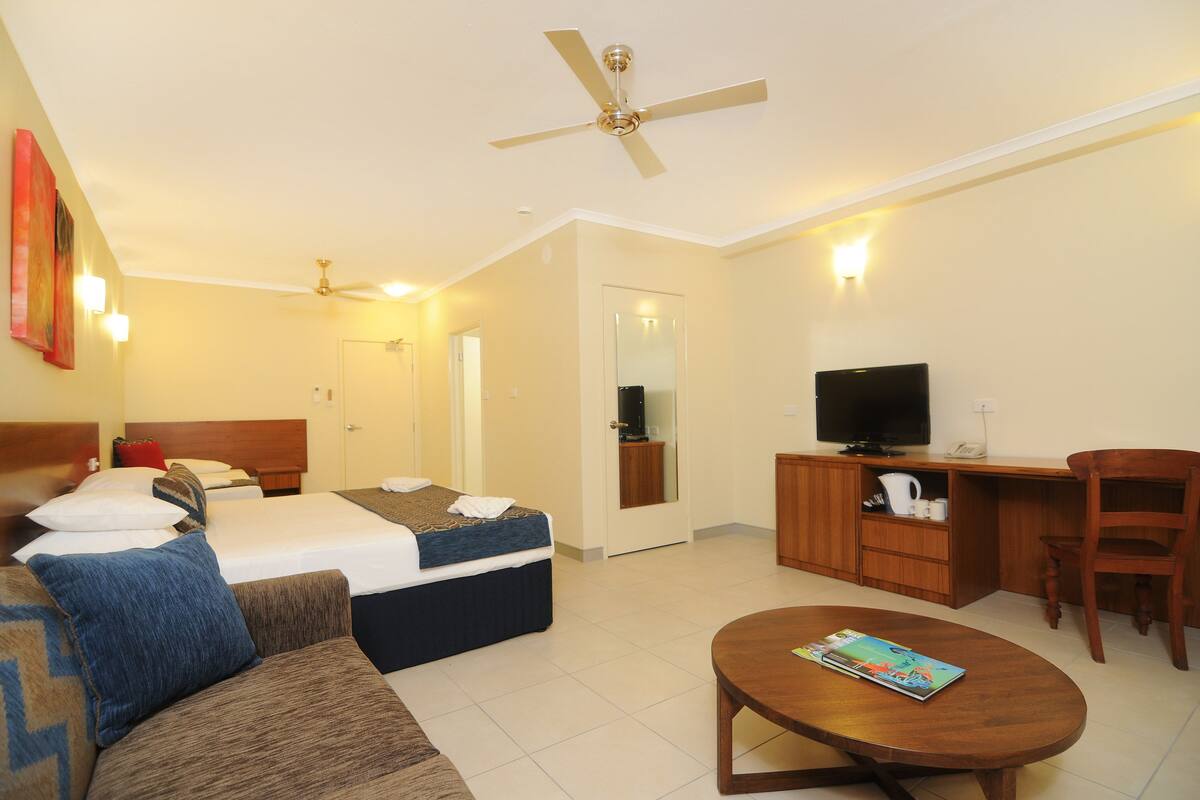 A hotel room with a bed, a sofa, a desk, a television, and a ceiling fan.