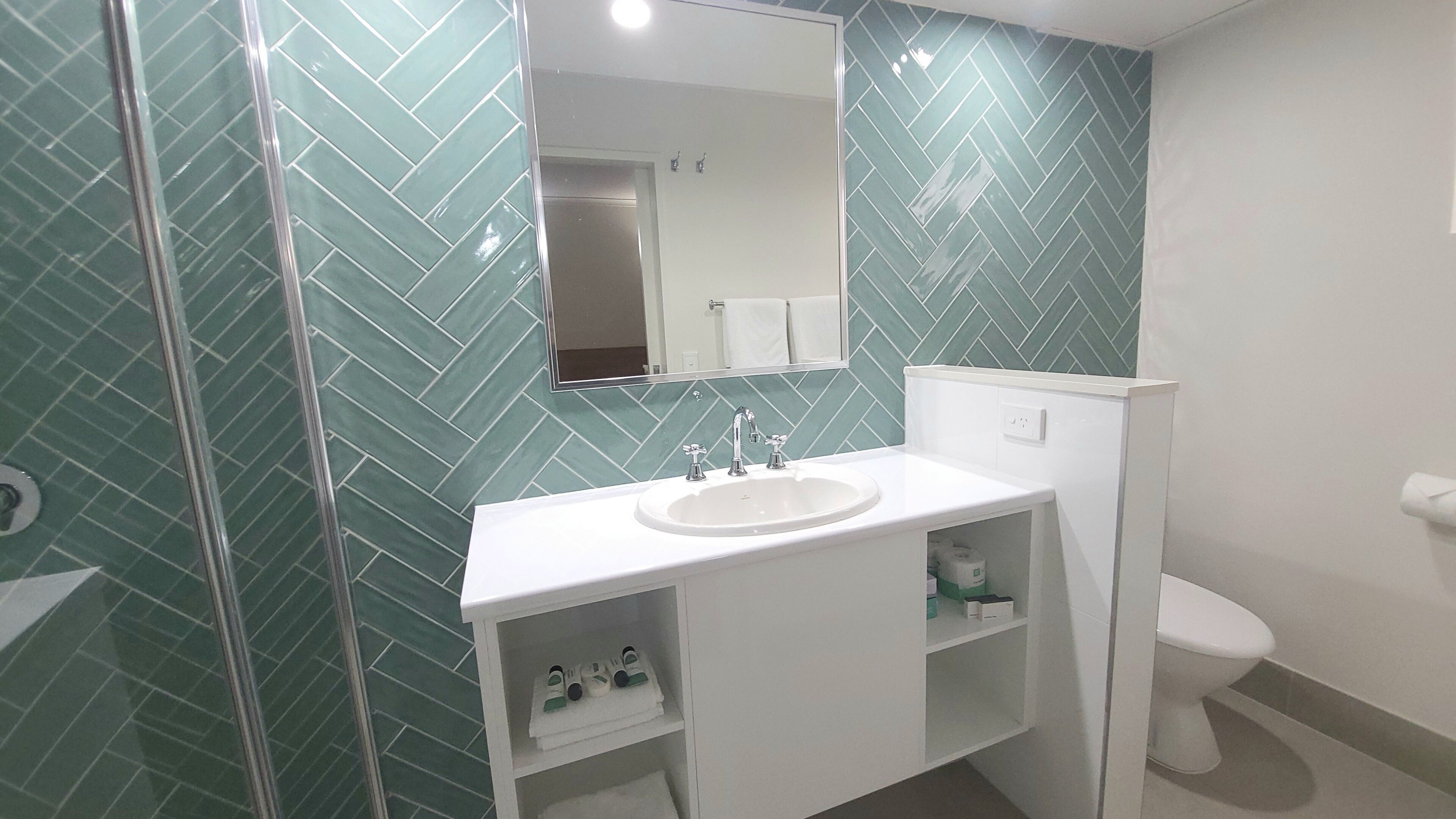 Casa de banho com lavatório branco, espelho e sanita.