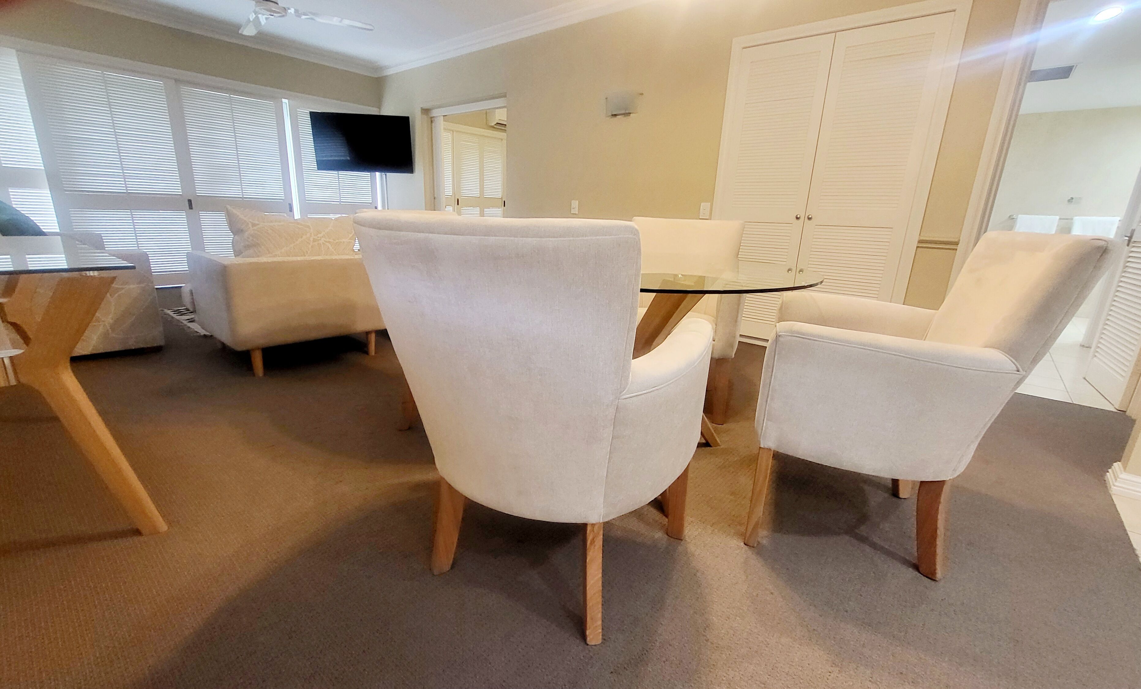 Una sala de estar moderna con una mesa de centro de vidrio, dos sillones blancos y un sofá.