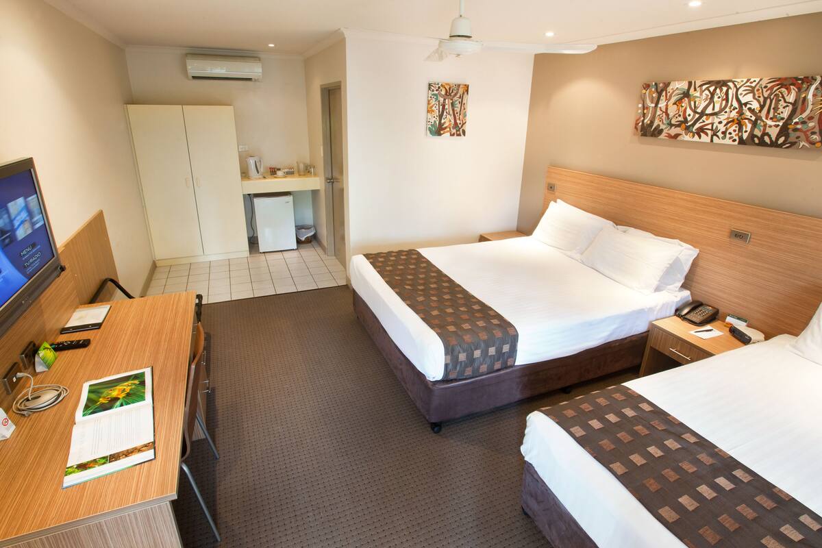A hotel room with two beds, a desk, a TV, and a small kitchenette.