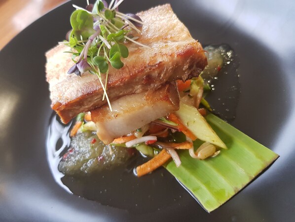 A dish with pork, vegetables, and a green leaf on a plate.