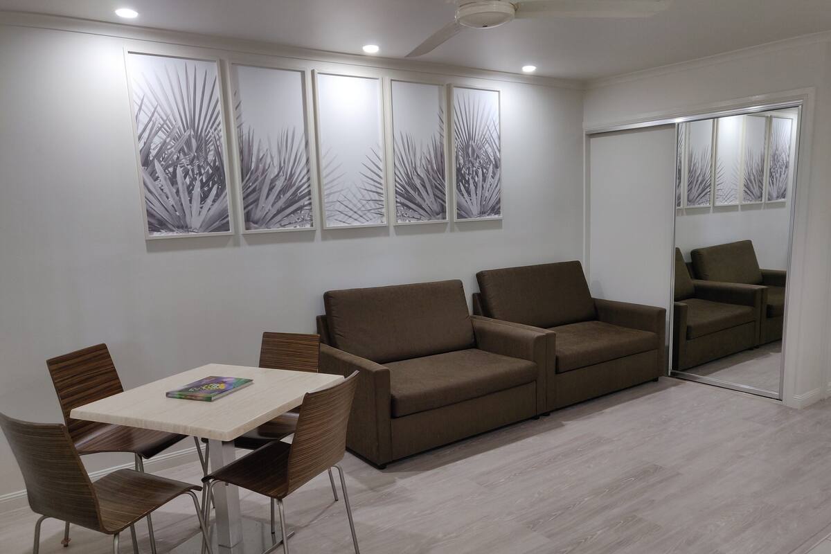 A modern living room with a brown sofa, a dining table with chairs, and a large mirror.