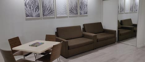 A modern living room with a brown sofa, a dining table with chairs, and a large mirror.