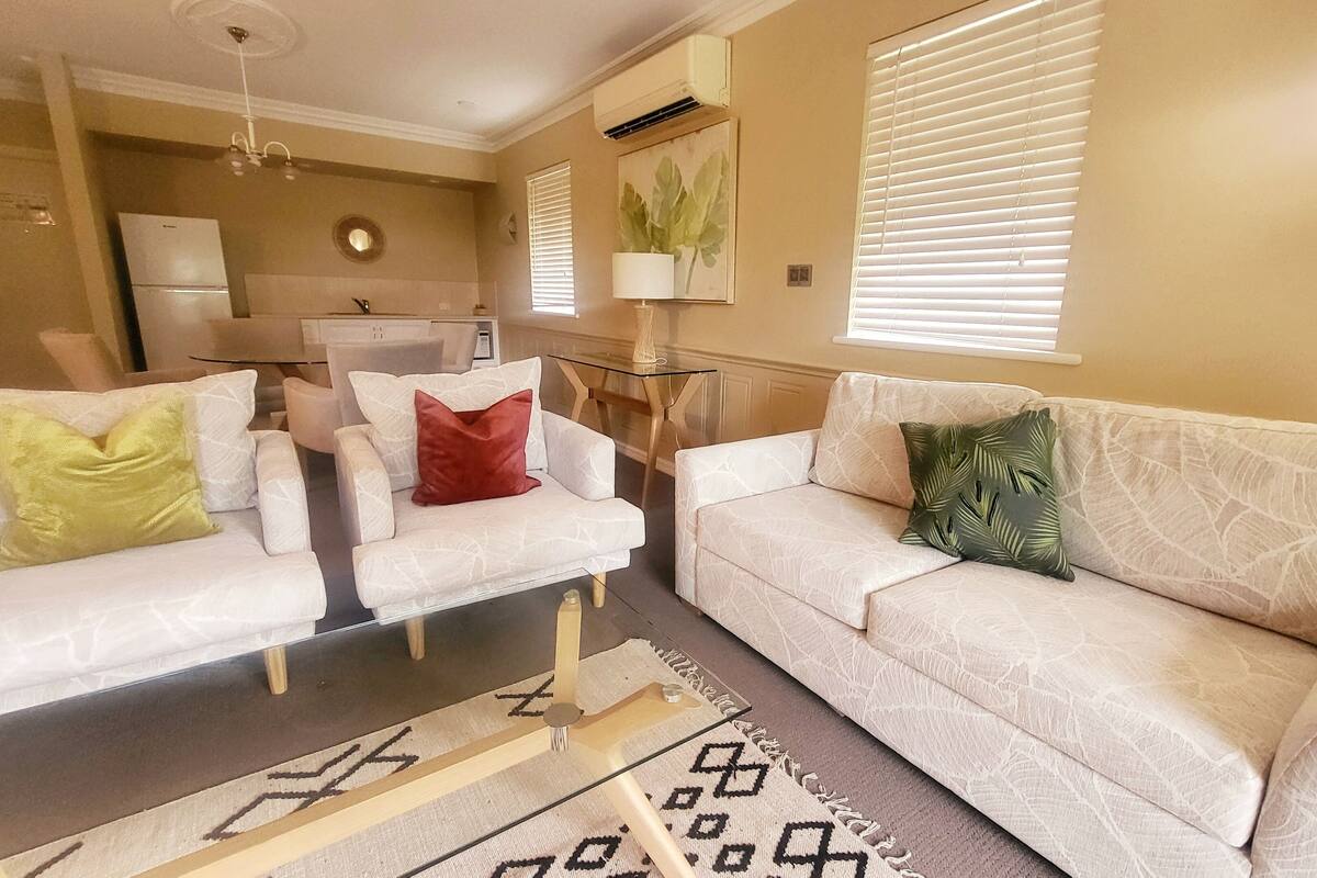 A living room with a sofa, armchairs, a glass coffee table, and a patterned rug.
