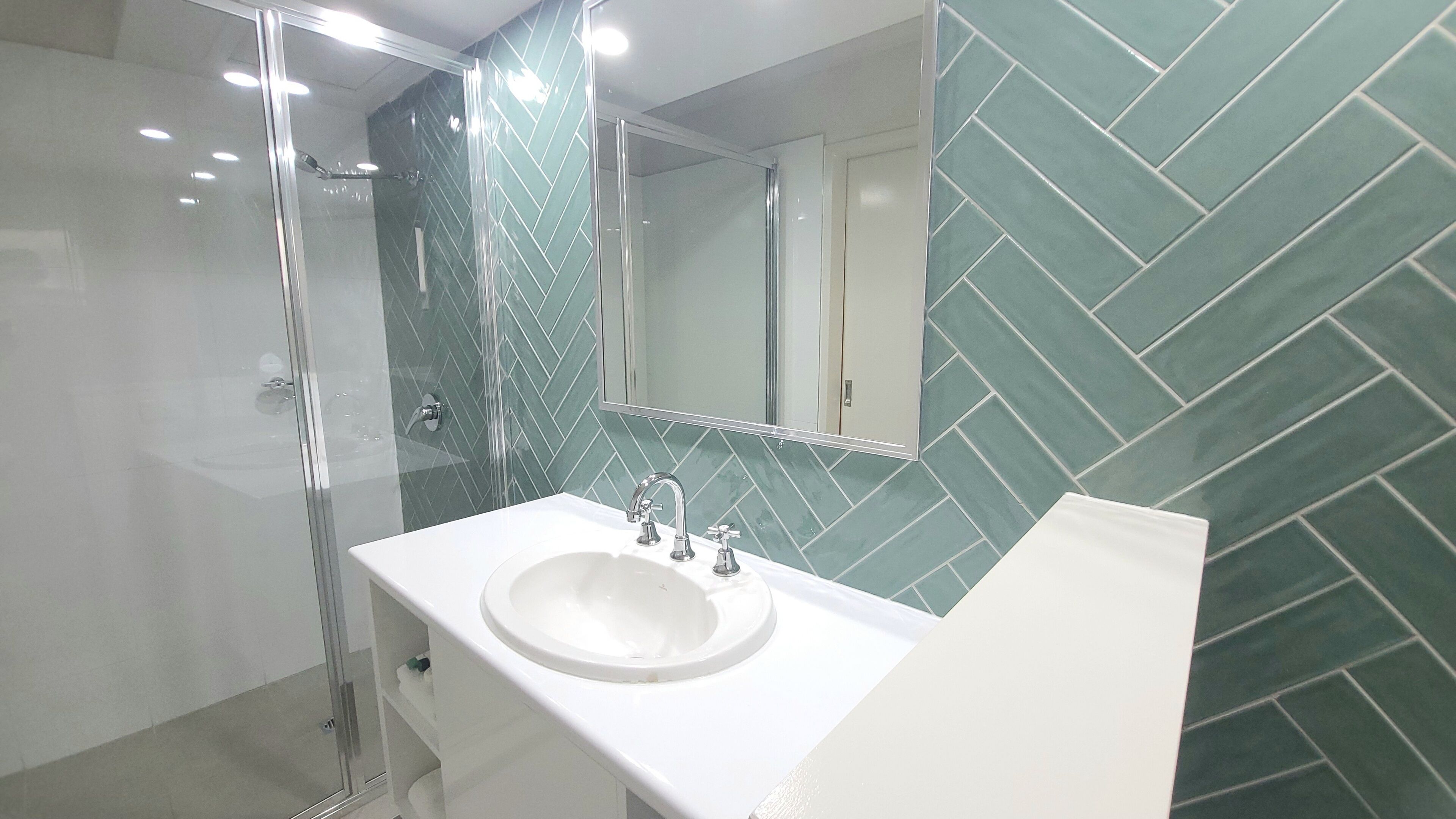 A bathroom with a glass-enclosed shower, a white sink with multiple faucets, and a mirror above the sink.