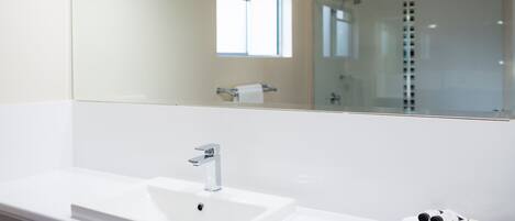 A modern bathroom with a large white sink, a mirror, and a glass shower enclosure.
