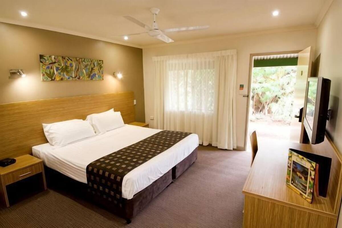 A hotel room with a bed, bedside table, TV, and a view of the outdoors.
