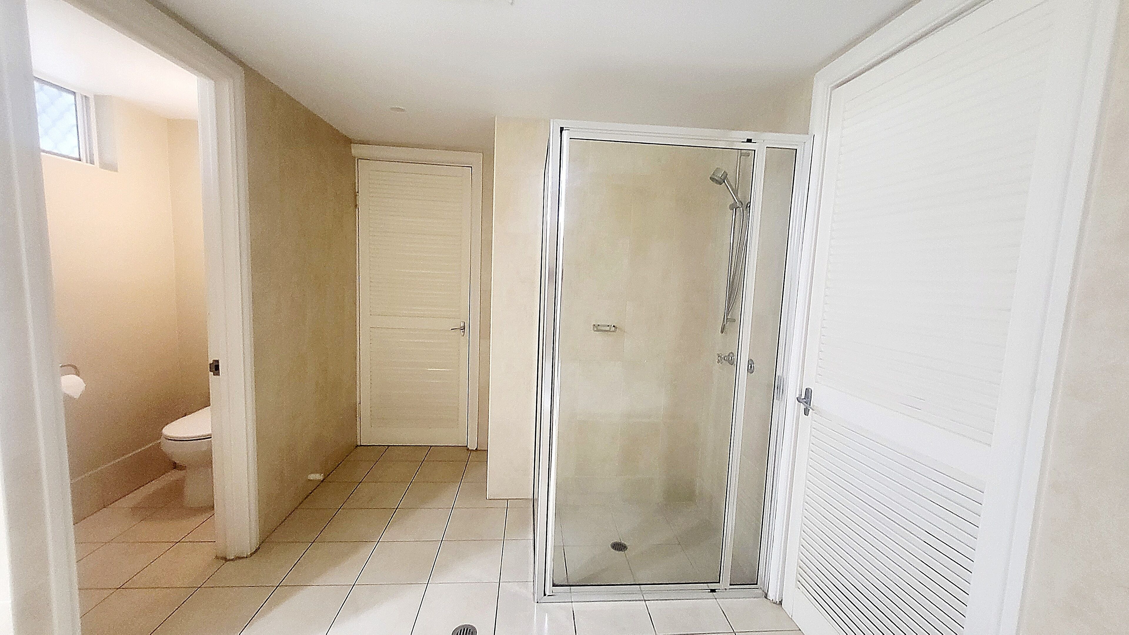 Ein Badezimmer mit Toilette, einer Dusche mit Glastür und einem gefliesten Boden.