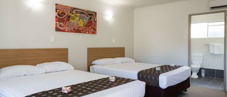 A hotel room with two single beds, a ceiling fan, a colorful artwork on the wall, and a bathroom with a toilet and sink.