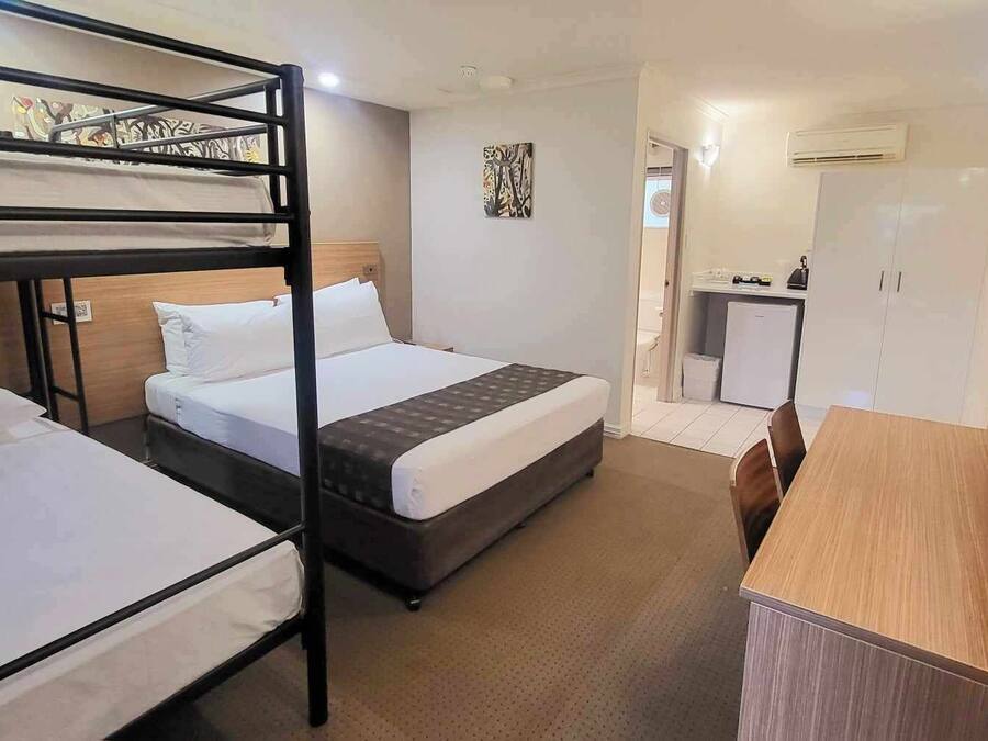 A hotel room with bunk beds, a single bed, a desk, a chair, a television, and a small kitchenette.