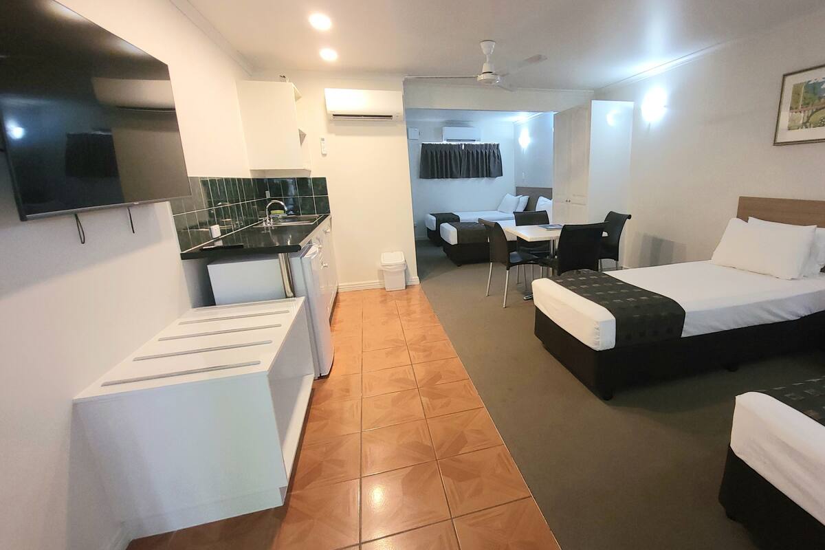 A hotel room with two beds, a kitchenette, a dining area, and a TV.