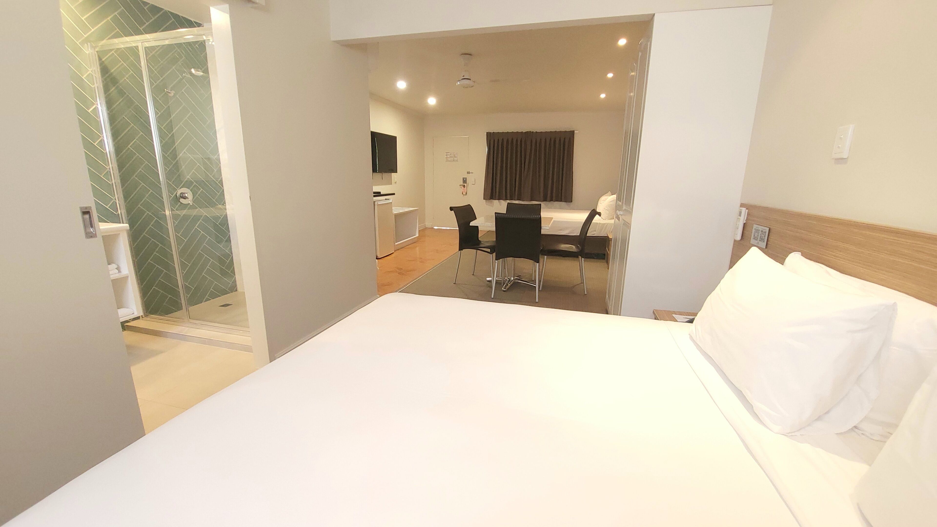 A hotel room with a bed, a shower, a dining area, and a TV.
