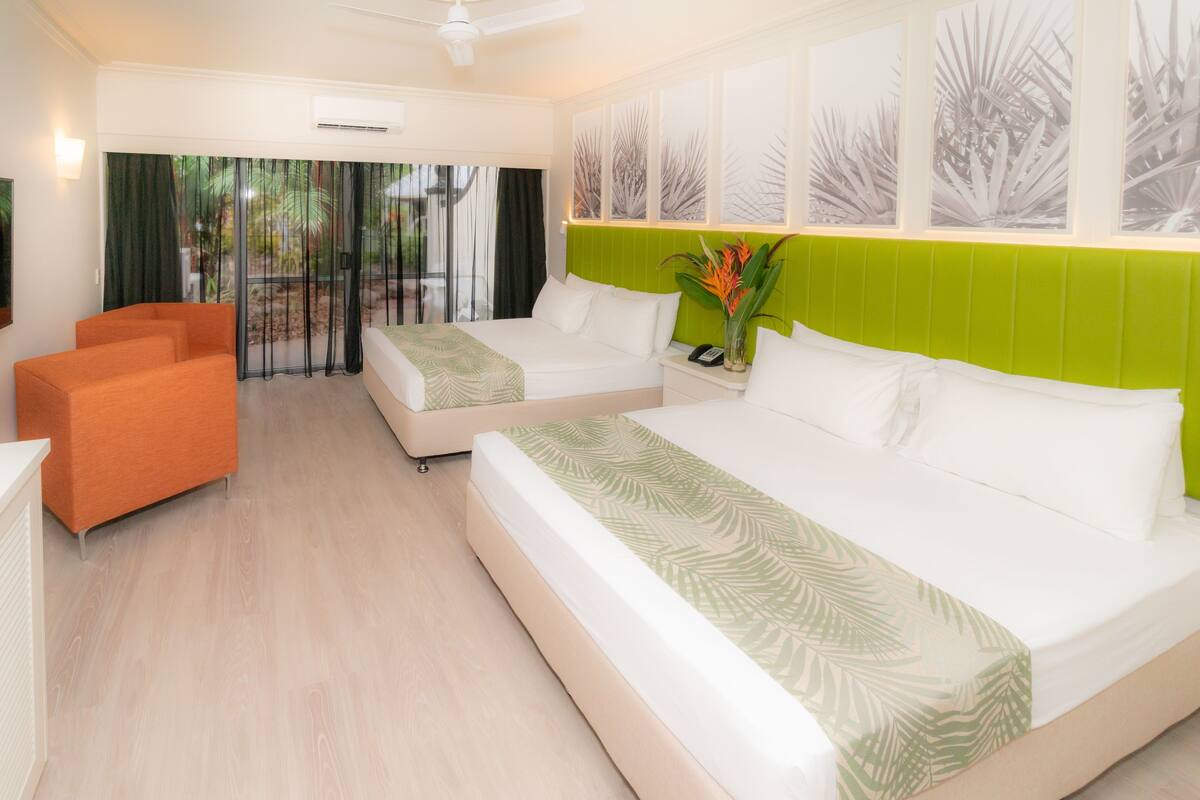 A hotel room with two beds, a sofa, and a view of palm trees through the window.