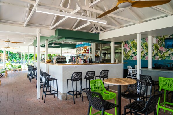 A restaurant with a bar area, green and black chairs, and a tropical-themed wall.