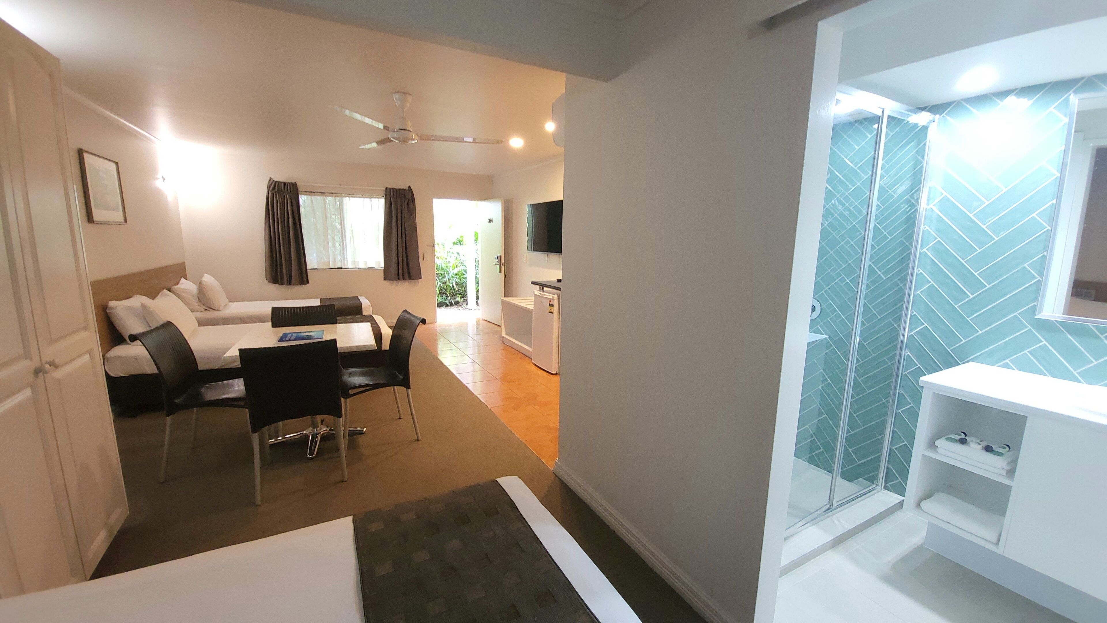 A modern hotel room with a dining area, a small kitchenette, and a shower with a glass enclosure.