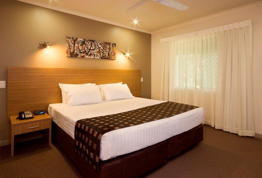 Habitación de hotel con una cama grande, una mesita de noche con teléfono, un ventilador de techo y una ventana con cortinas.
