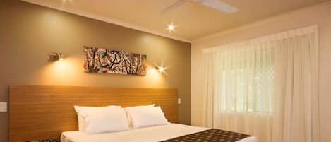 Quarto de hotel com uma cama grande, mesa de cabeceira com telefone, ventilador de teto e janela com cortinas.