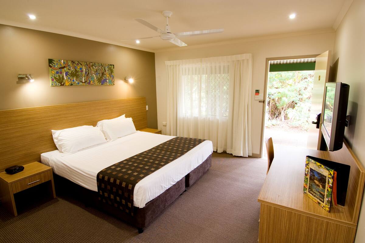 A hotel room with a bed, bedside table, and a desk with a book.