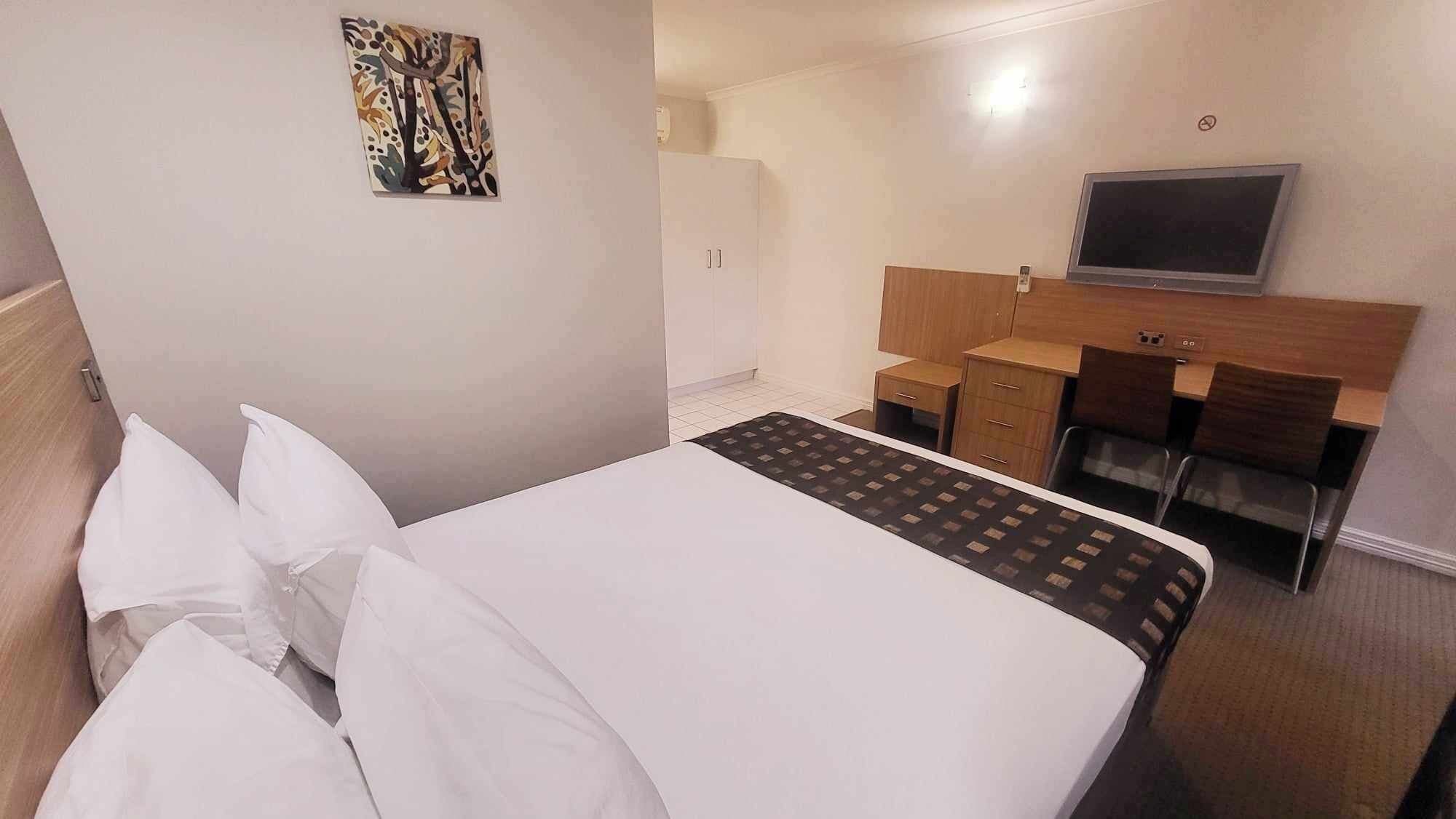Una habitación de hotel con cama, escritorio, silla, televisión y armario.
