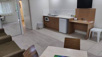 Una cocina moderna con microondas, refrigerador y televisor de pantalla plana en la pared. Cuenta con un comedor con mesa y sillas, además de un taburete blanco.
