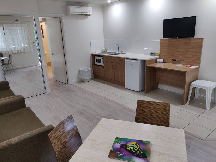 Una cocina moderna con microondas, refrigerador y televisor de pantalla plana en la pared. Cuenta con un comedor con mesa y sillas, además de un taburete blanco.