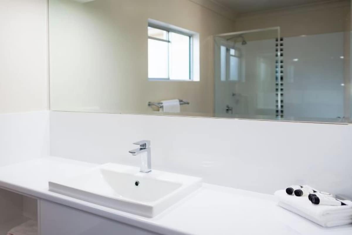 A modern bathroom with a large white sink, a mirror, and a glass shower enclosure.