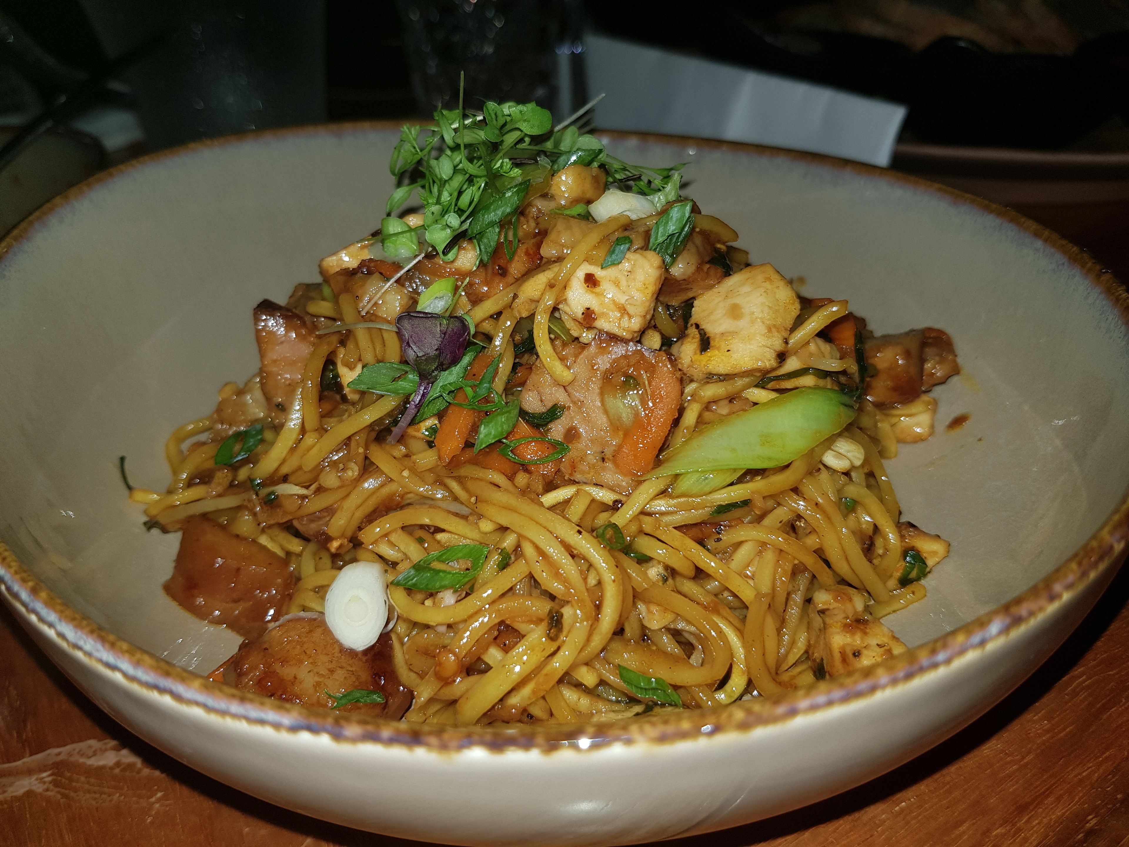 Un tazón de fideos con verduras y carne, adornado con hierbas.