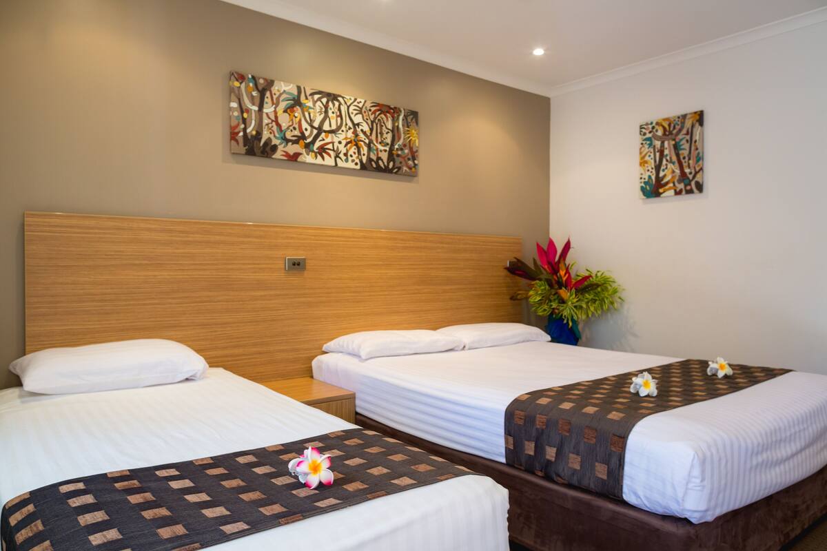 A hotel room with two single beds, a wooden headboard, and two abstract paintings on the walls.