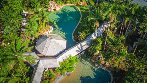 An aerial view of a resort with a swimming pool, palm trees, and a covered walkway. - Cairns Colonial Club Resort (Manunda)