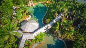 An aerial view of a resort with a swimming pool, palm trees, and a covered walkway.