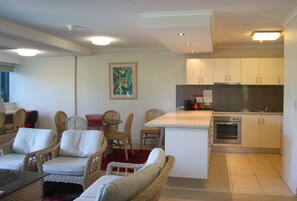 Una sala de estar con muebles de mimbre, una mesa de comedor y una cocina con alacenas blancas y una estufa.