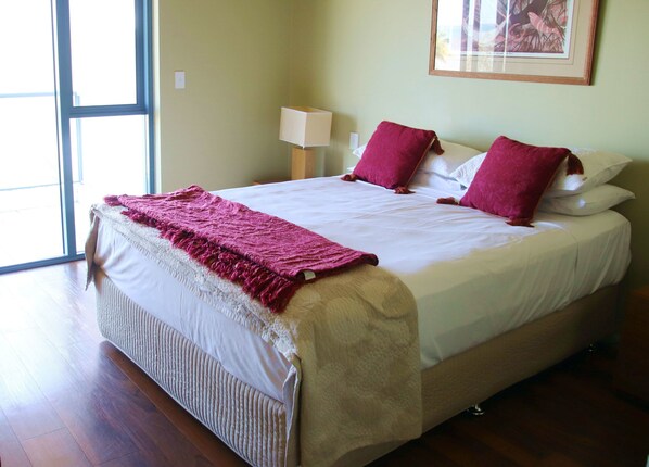 A neatly made bed with a white and beige duvet, two red pillows, and a pink throw blanket.