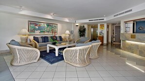A spacious living area with a sofa set, wicker chairs, a coffee table, and a reception desk. - 181 The Esplanade (Cairns North)