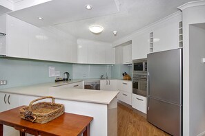 Une cuisine moderne avec des meubles blancs, un réfrigérateur en acier inoxydable et une table à manger en bois agrémentée d’un panier.
