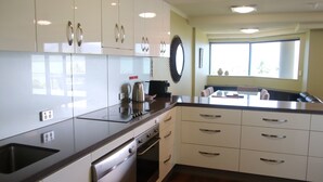 A modern kitchen with white cabinets, stainless steel appliances, and a large window providing natural light. - 181 The Esplanade (Cairns North)