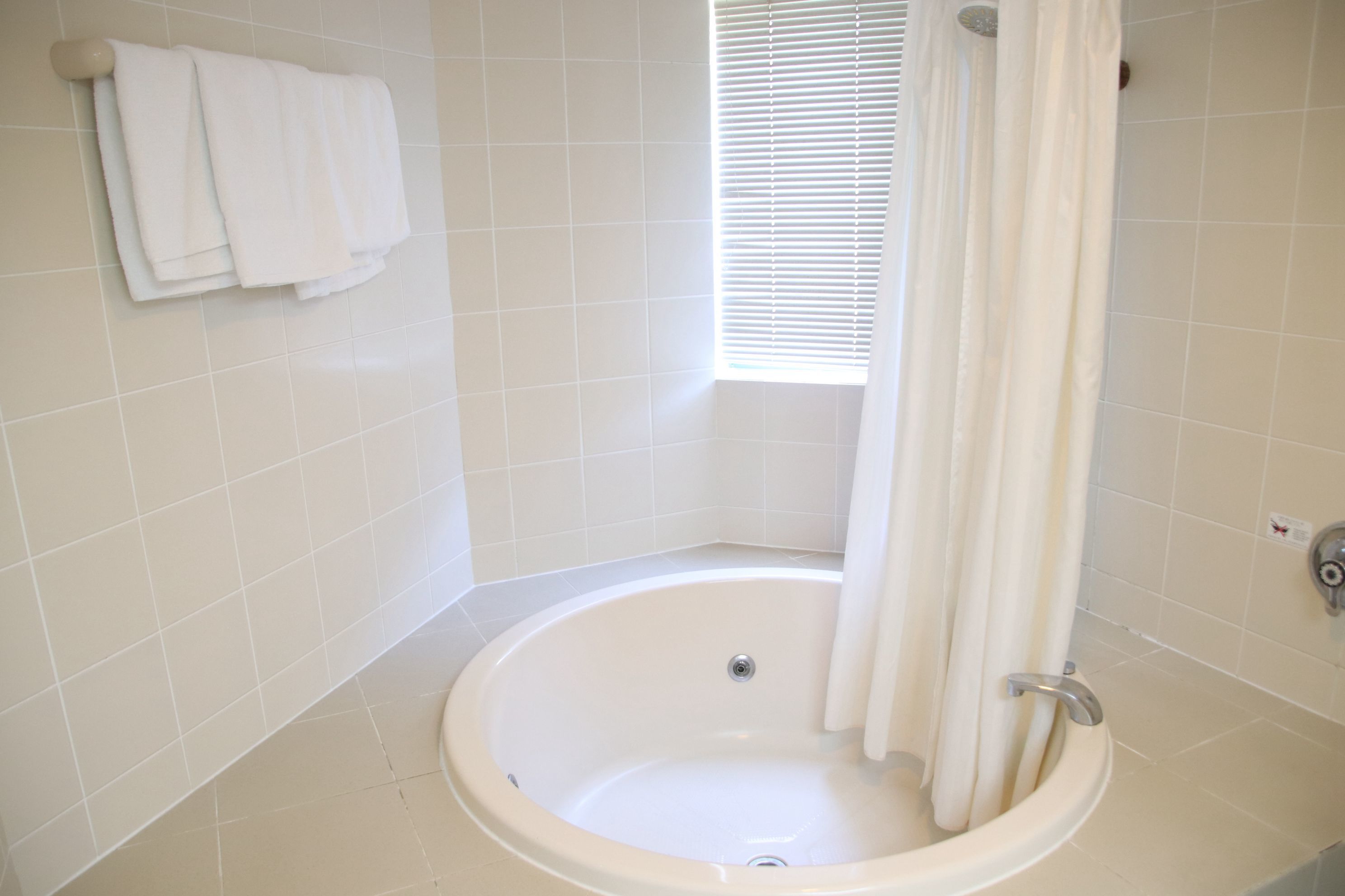A bathroom with a bathtub, a window with blinds, and a towel rack with towels.