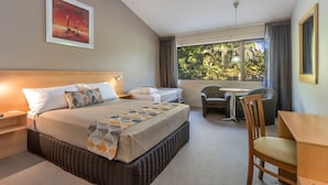 A hotel room with a large bed, a desk, a chair, and a window with a view of trees.