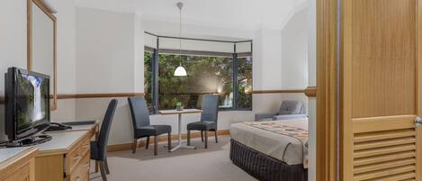 A hotel room with a bed, desk, chair, TV, and a large window with a view of greenery.
