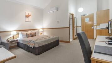 A hotel room with a bed, bedside table, lamp, desk, chair, and a small kitchenette area.