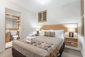 A hotel room with a large bed, two bedside tables with lamps, a headboard, a mirror, a toilet, and a shower area. - Airport International Hotel Brisbane (Hamilton)
