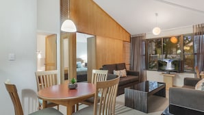 A modern living room with a wooden staircase, a dining area with a round table and chairs, a sofa, and a TV on a stand.