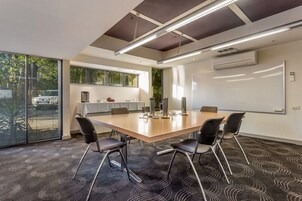 Un salón de conferencias con una gran mesa, cuatro sillas, una pizarra y un amplio ventanal con persianas.