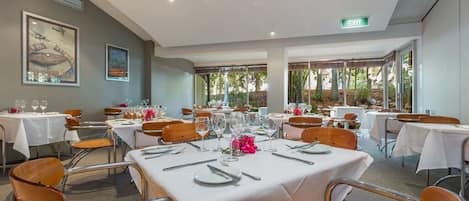Un comedor con mesas dispuestas para una comida, sillas y vistas al exterior.