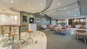 A modern dining area with round tables and bar stools, a curved ceiling, and framed artwork on the walls.