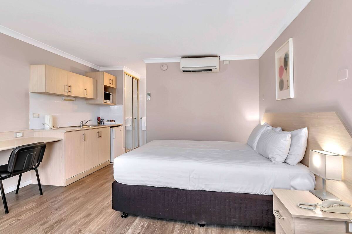 A hotel room with a bed, bedside table, desk, and kitchenette.