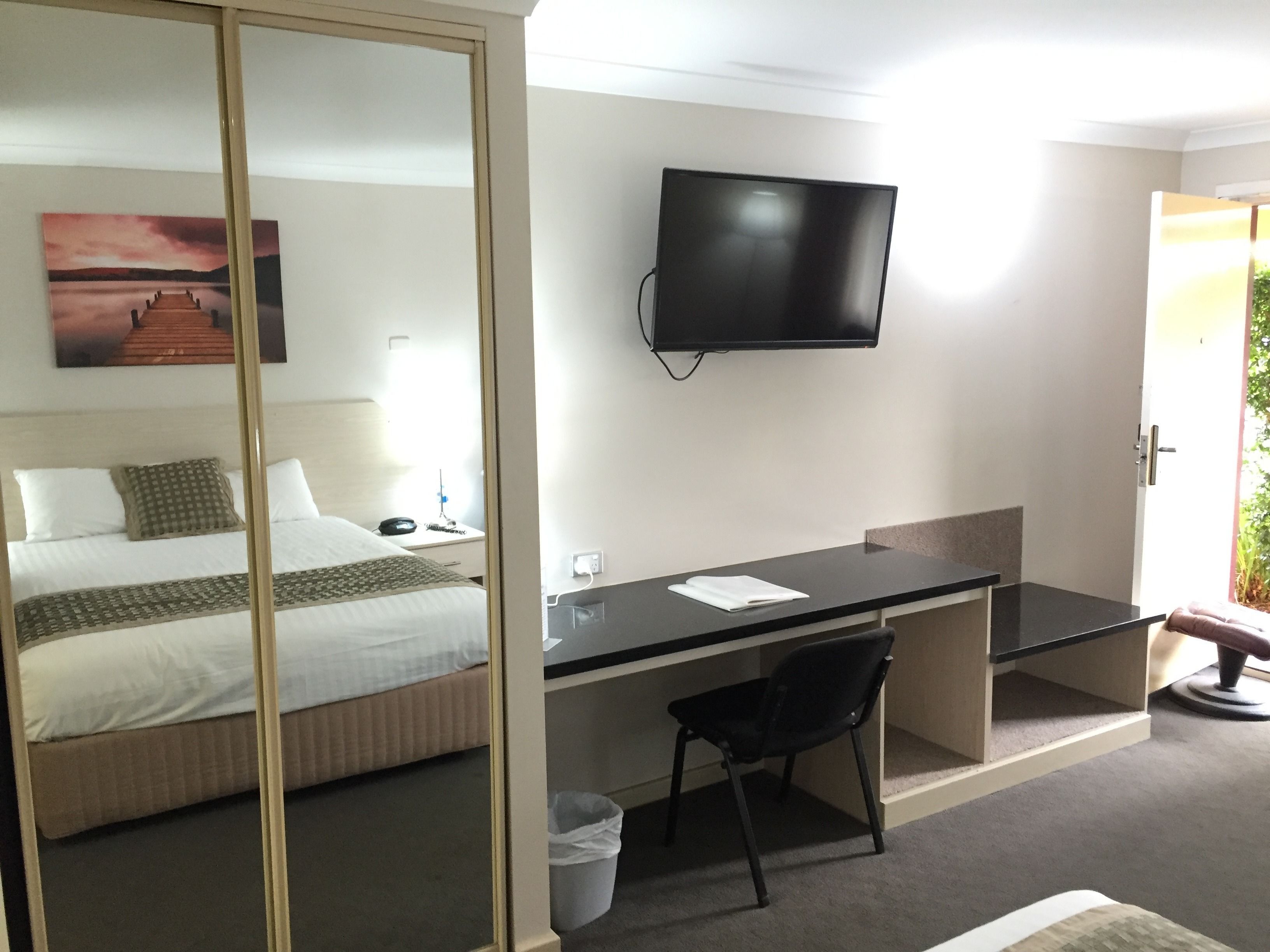 Ein Hotelzimmer mit einem Bett, einem Schreibtisch, einem Sessel, einem Fernseher und einem Bild an der Wand.