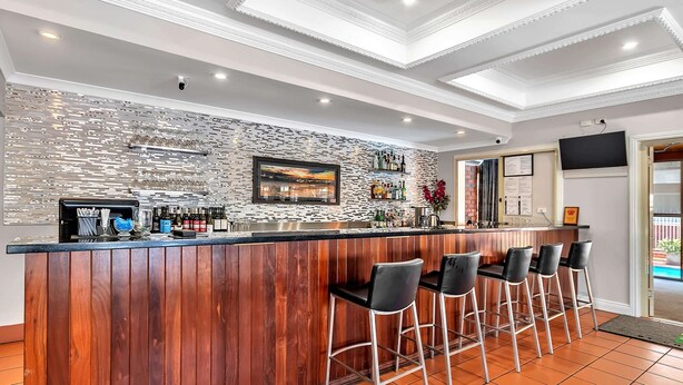 Una zona de bar con mostrador de madera, taburetes, una pared decorativa y un televisor.