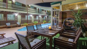 Un área de descanso al aire libre con varios niveles, piscina, mobiliario de madera y una mesa de comedor lista para una comida.